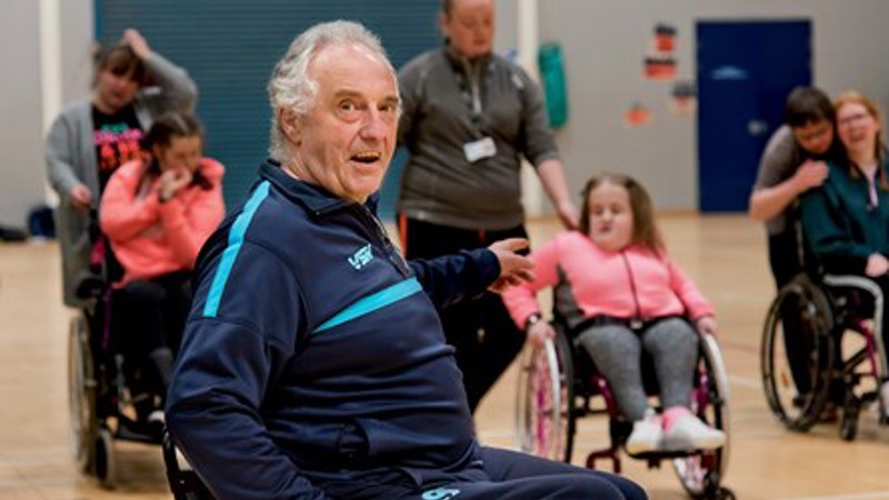 A person wears a navy blue sports jumper and sits in a wheelchair.